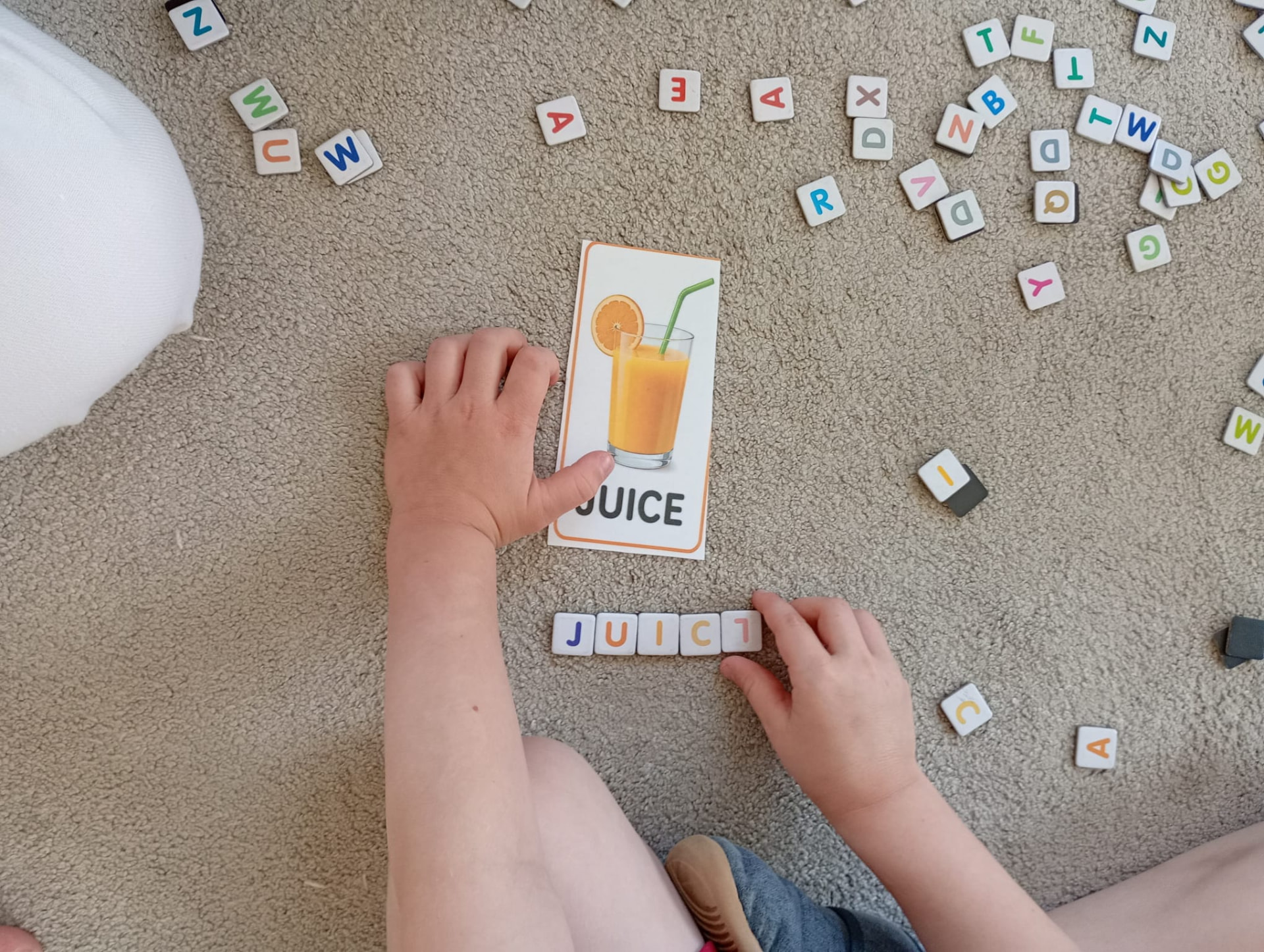 Dziecko układające słowo JUICE z literowych kostek przy karcie obrazkowej